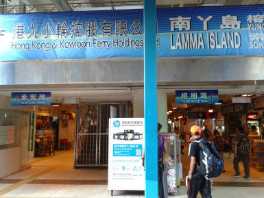 Entrance to Yung Shue Wan ferry pier on Lamma Island with signage, shops, and arriving passengers